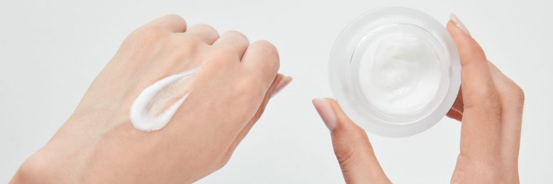 panoramic shot of woman applying cream on skin and holding jar isolated on white